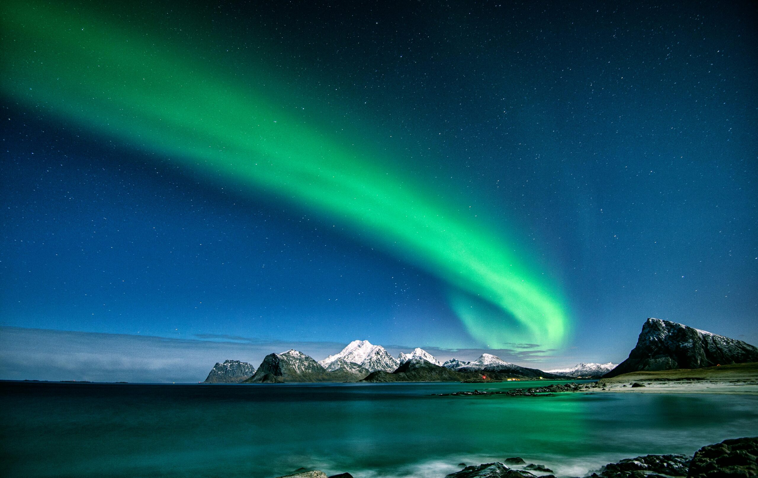 Breathtaking view of the Northern Lights over snow-capped mountains in Lofoten, Norway.